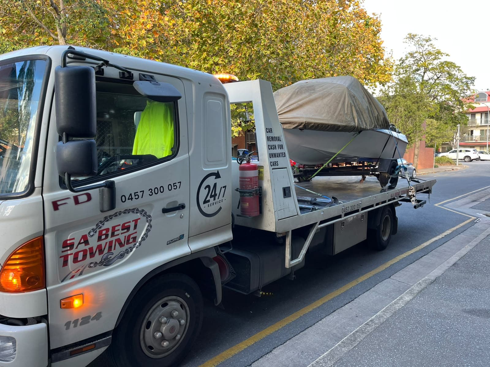 The SA Best Towing Hino with its hazard lights and amber light bar on, a covered boat on its trailer loaded on the tray