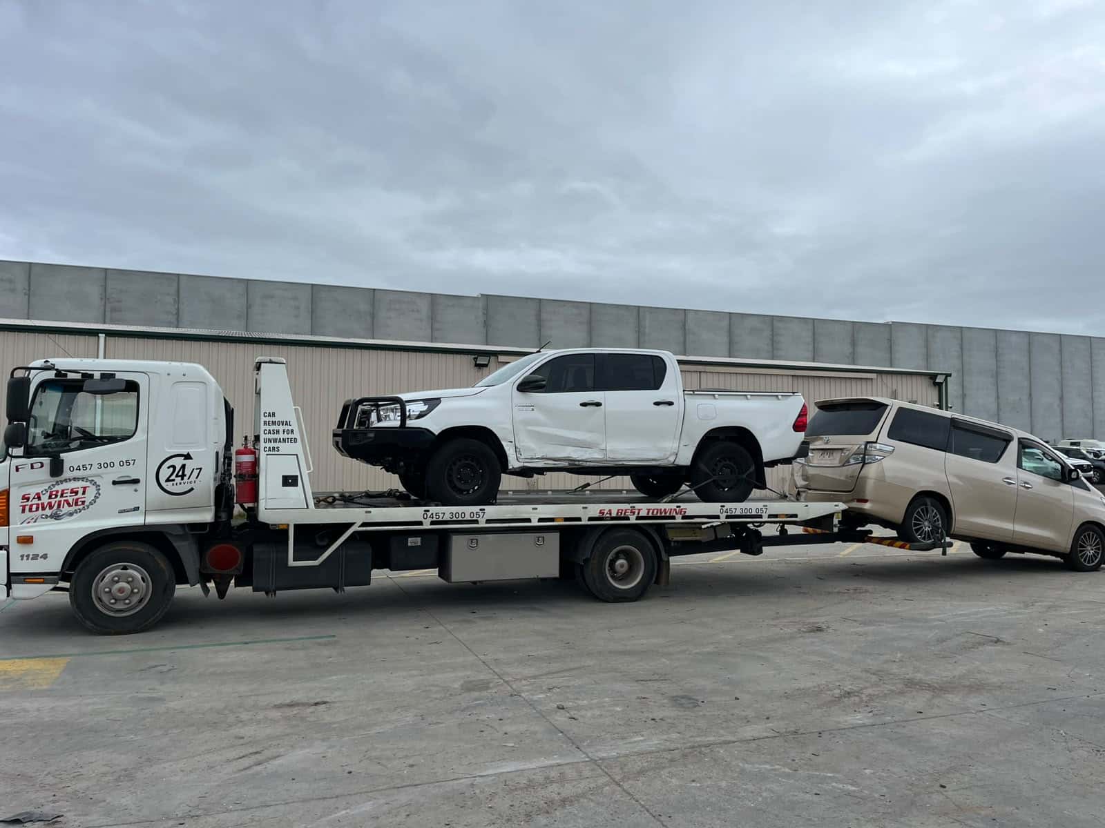White Toyota HiLux with its side doors pushed in on the SA Best Towing tray, a champagne Toyota people mover towed behind on the rear lift