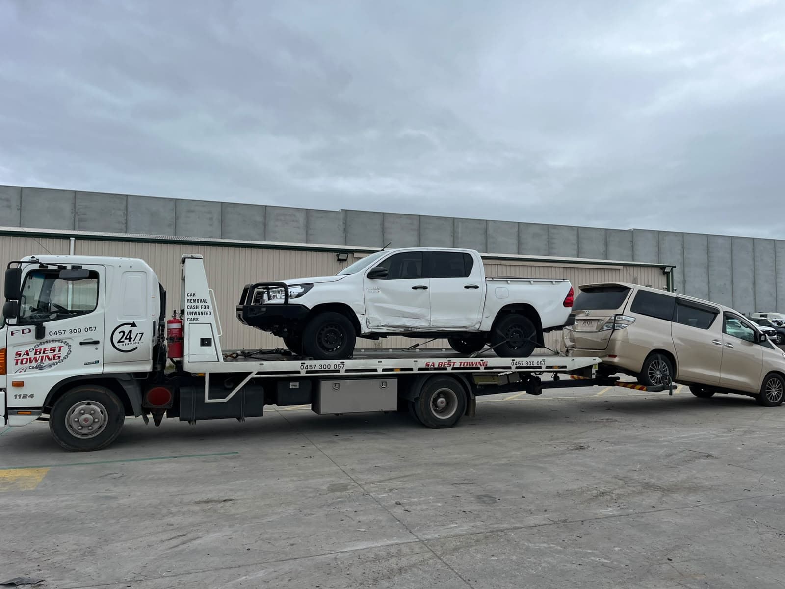 Damaged HiLux on the tray with a people mover on the rear lift
