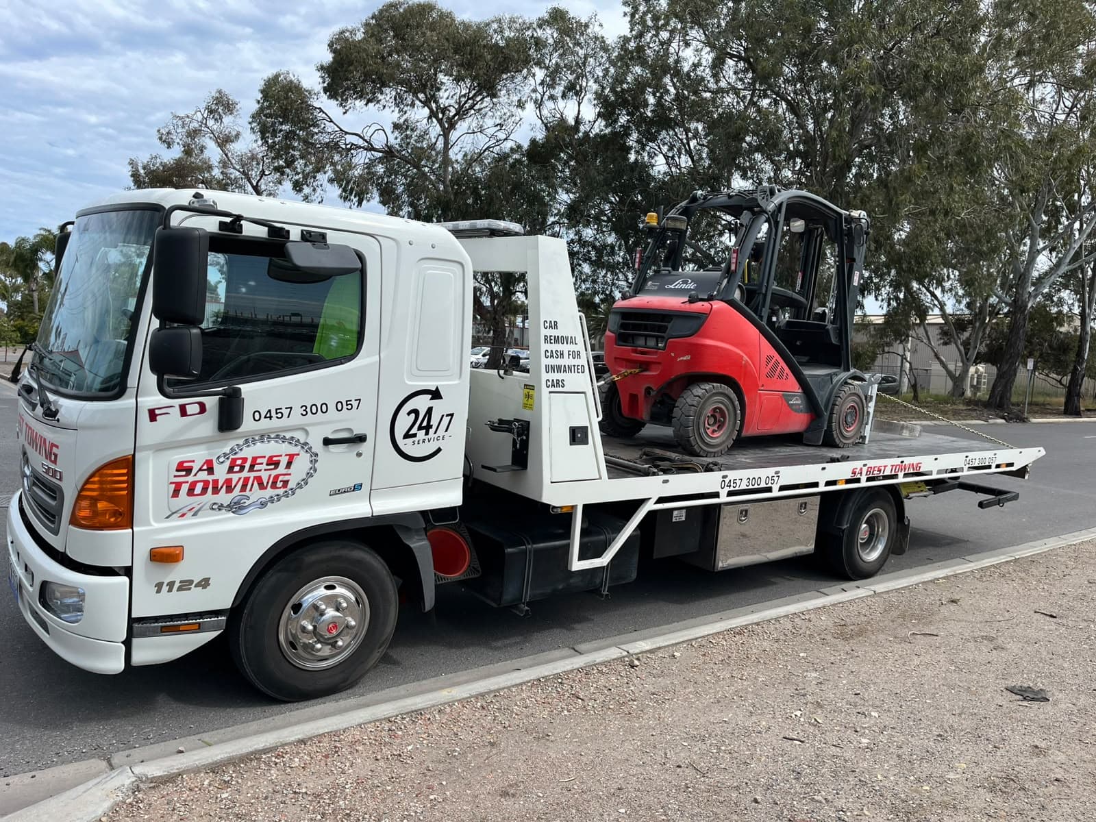 Red Linde forklift chained on the SA Best Towing Hino tilt tray, counterweight towards the cab, on a street lined with gum trees