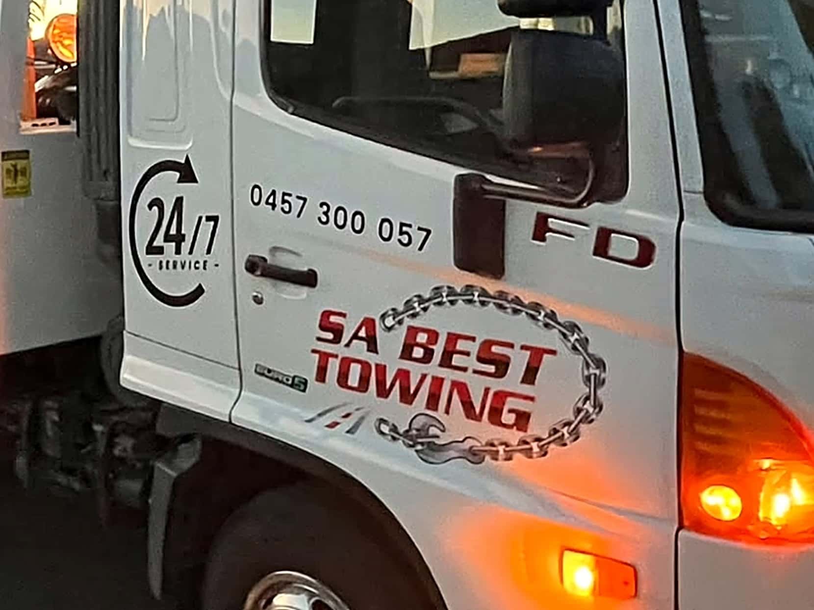 SA Best Towing’s white Hino tilt tray at dusk, its amber lights on