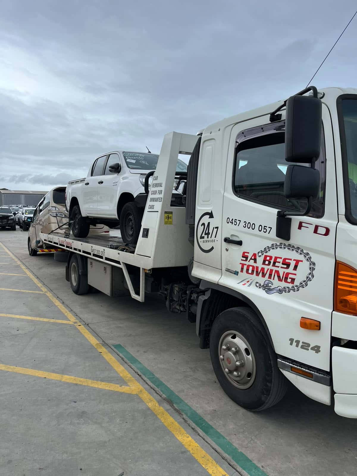 White Toyota HiLux on the SA Best Towing tray with the champagne people mover from the same job on the rear lift, rows of parked cars behind