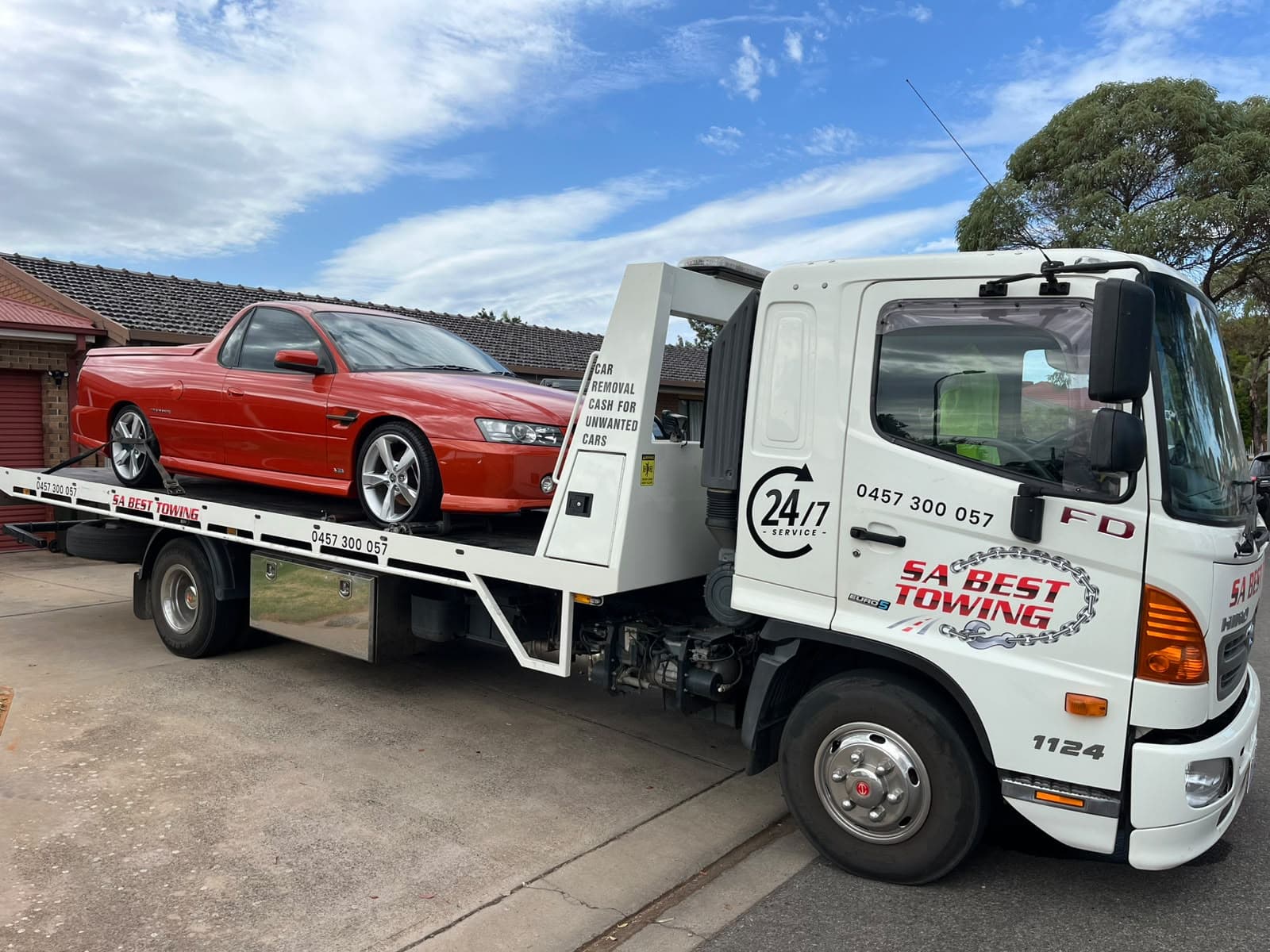Red Holden Commodore ute with a tonneau cover strapped on the SA Best Towing tilt tray in a residential driveway
