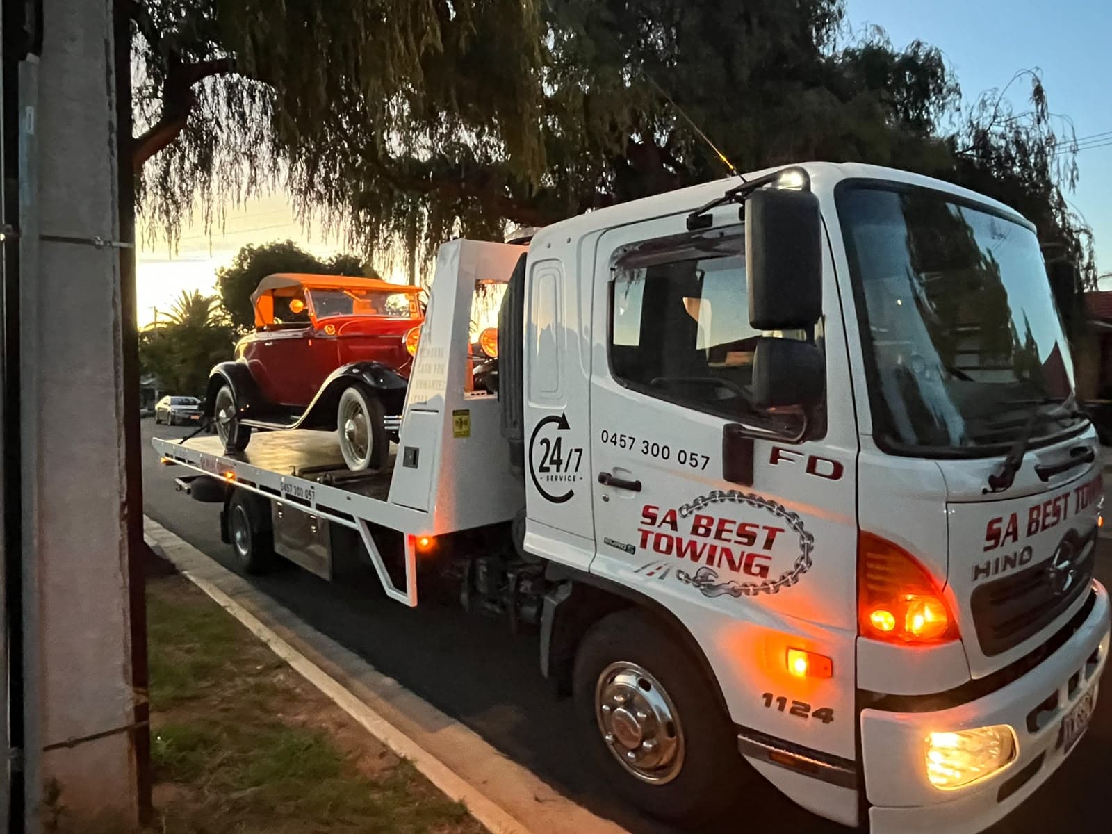 SA Best Towing’s white Hino tilt tray at dusk with a red 1930s-style roadster strapped on the tray
