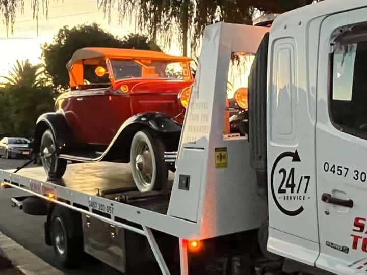 Close view of a red roadster with black guards, a tan soft top and whitewall tyres strapped on the SA Best Towing tray at dusk