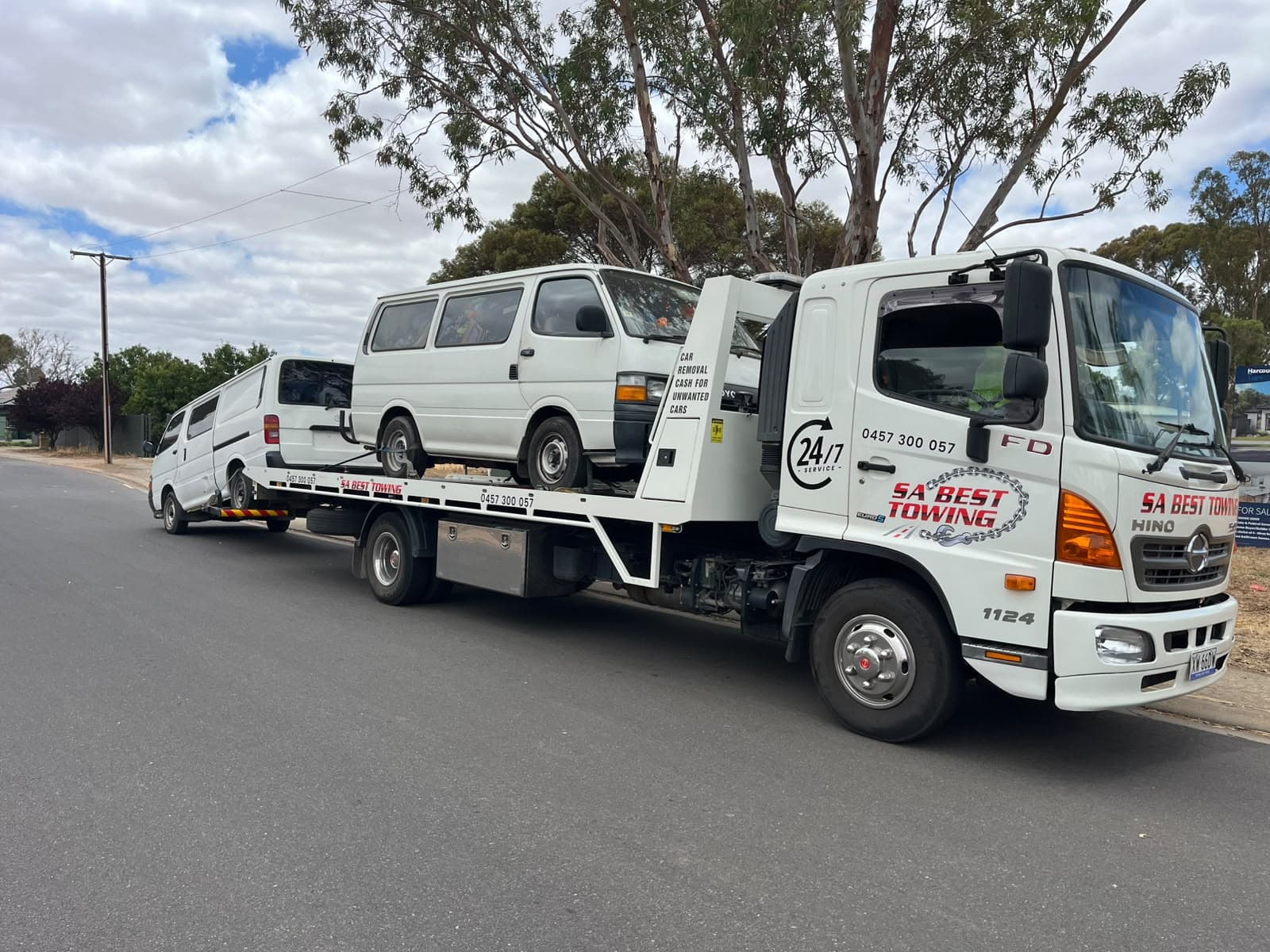 White Toyota HiAce van on the SA Best Towing tilt tray, a second white van on the rear lift, gum trees along the road